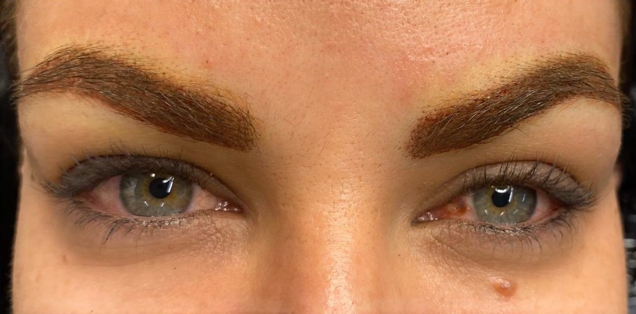 The same eyes straight after permanent makeup: full, arched brows in warm brown with fine hair strokes.