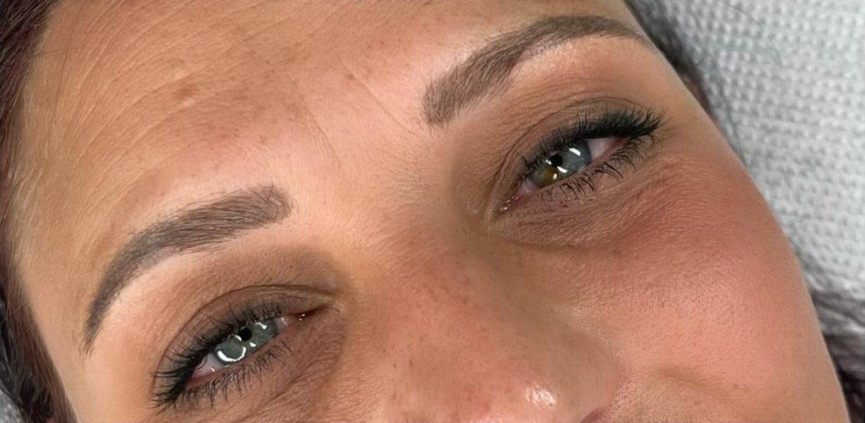 A client lying back before permanent makeup: soft, uneven brows.