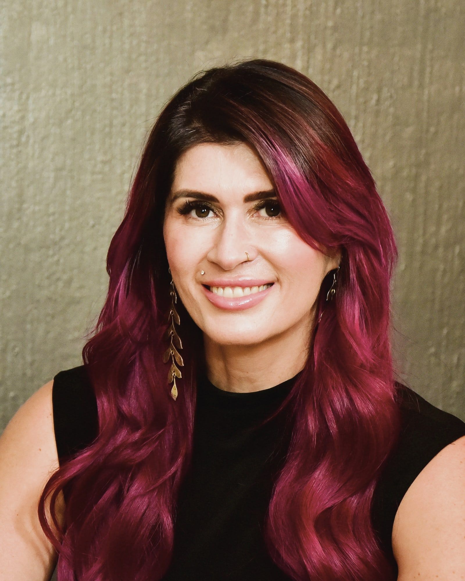 Marguerite, who runs Beauty Connection, smiling in the studio, with long magenta hair.